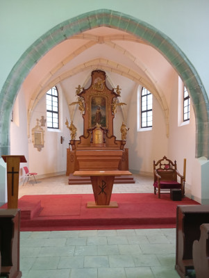Presbytář kostela Narození sv. Jana Křtitele / Presbytář je sklenut jedním polem křížové žebrové klenby a parsčitě v závěru na kuželovité profilované konzoly. V severní stěně je pozdně gotický výklenkový sanktuář v kamenném rámci s křížovou kytkou a kraby. Vedle sanktuáře je kamenná polopostava Krista s kalichem, do něhož prýští krev.